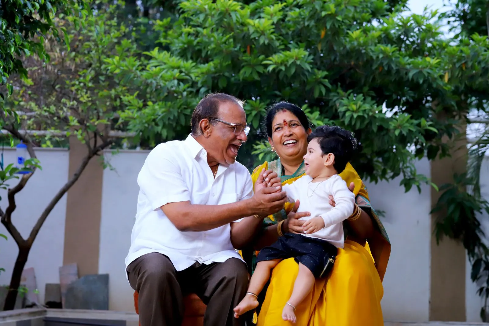An older Indian couple laughing with their baby grandson in the garden