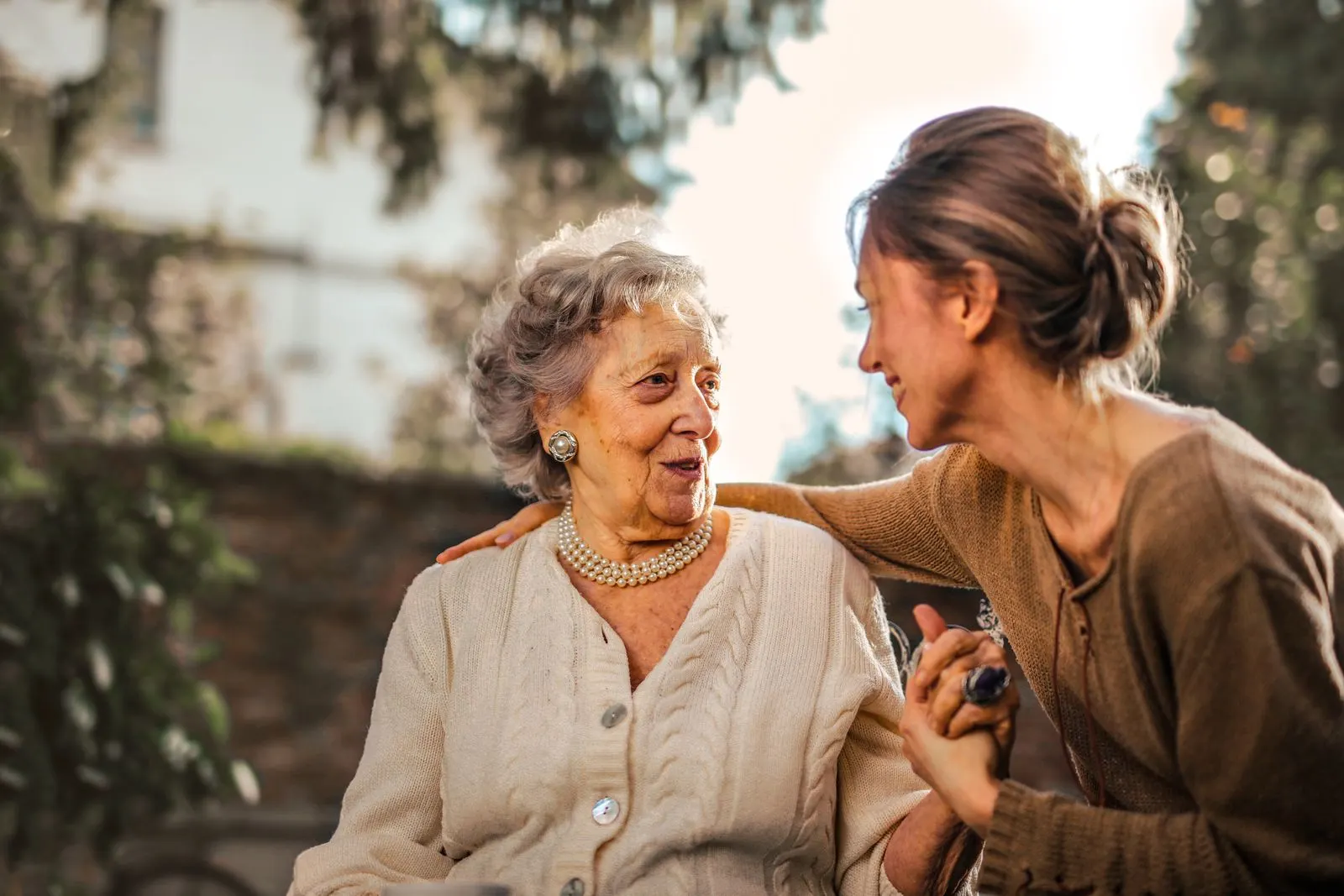 A younger woman holding an older woman's hand as they laugh together in the garden