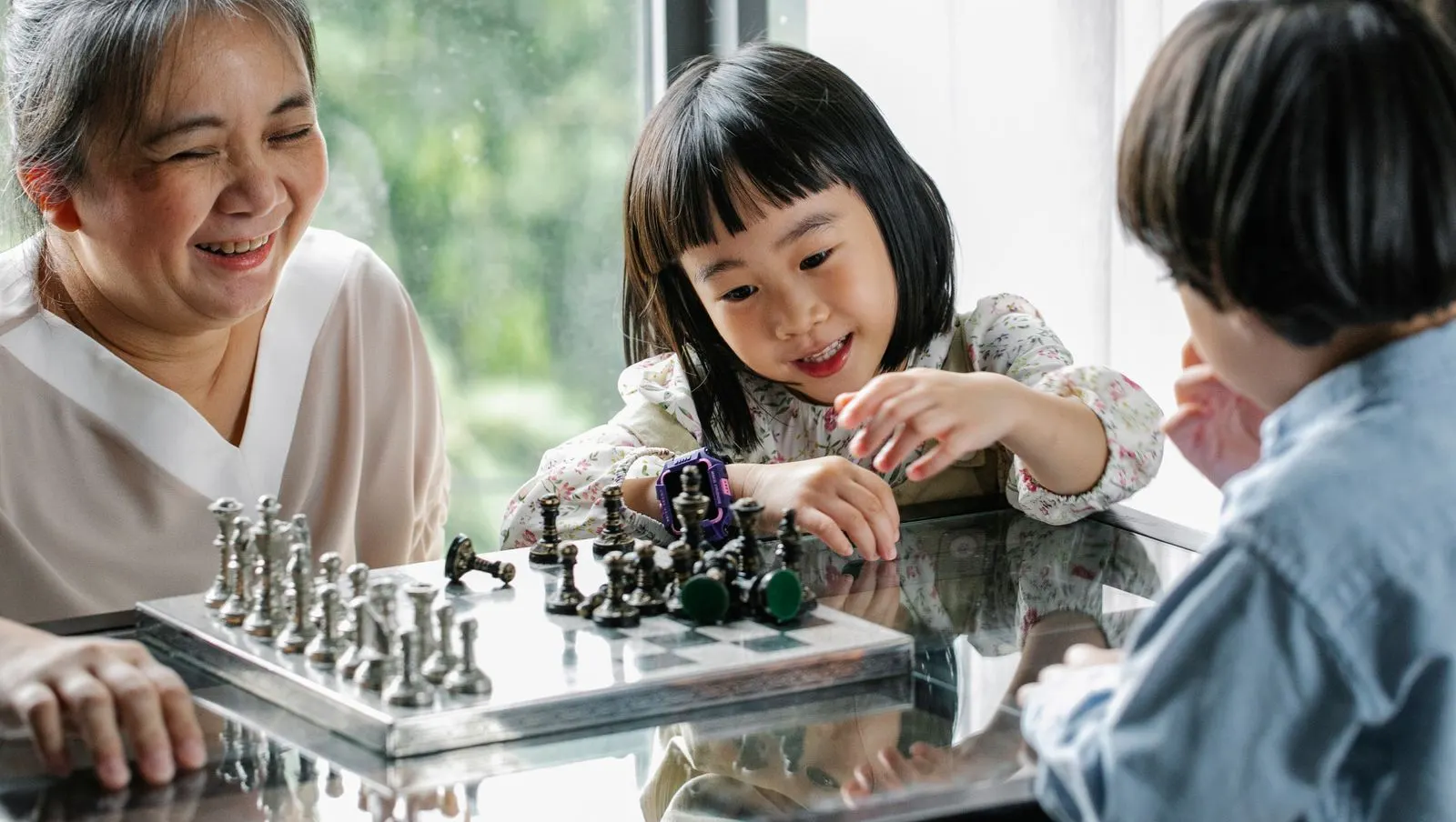 A grandmother laughing as she plays chess with her grandchildren
