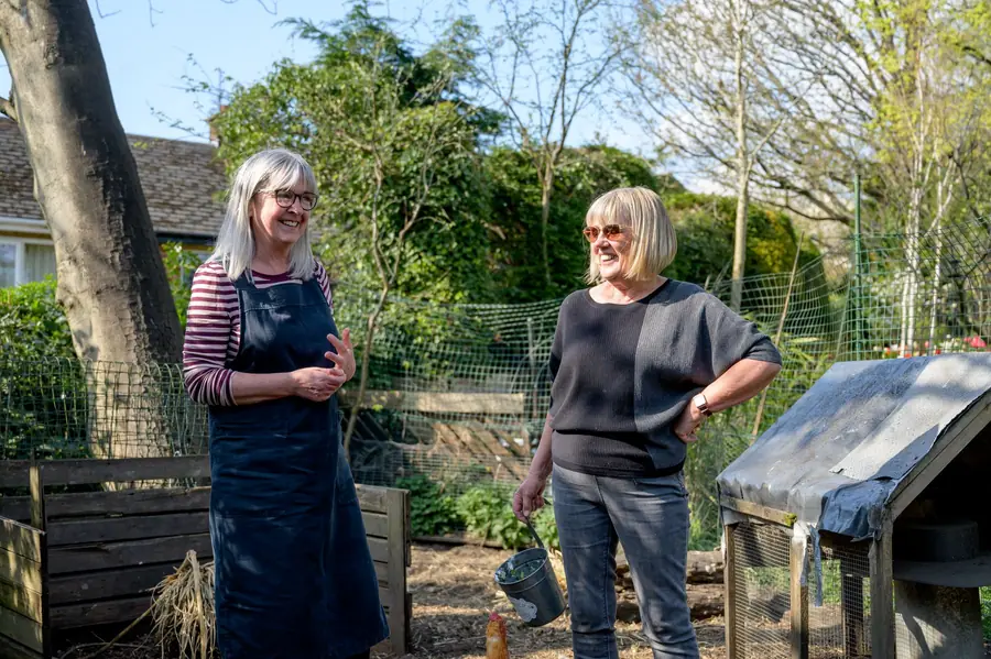 Two older women smiling and talking in a backyard garden