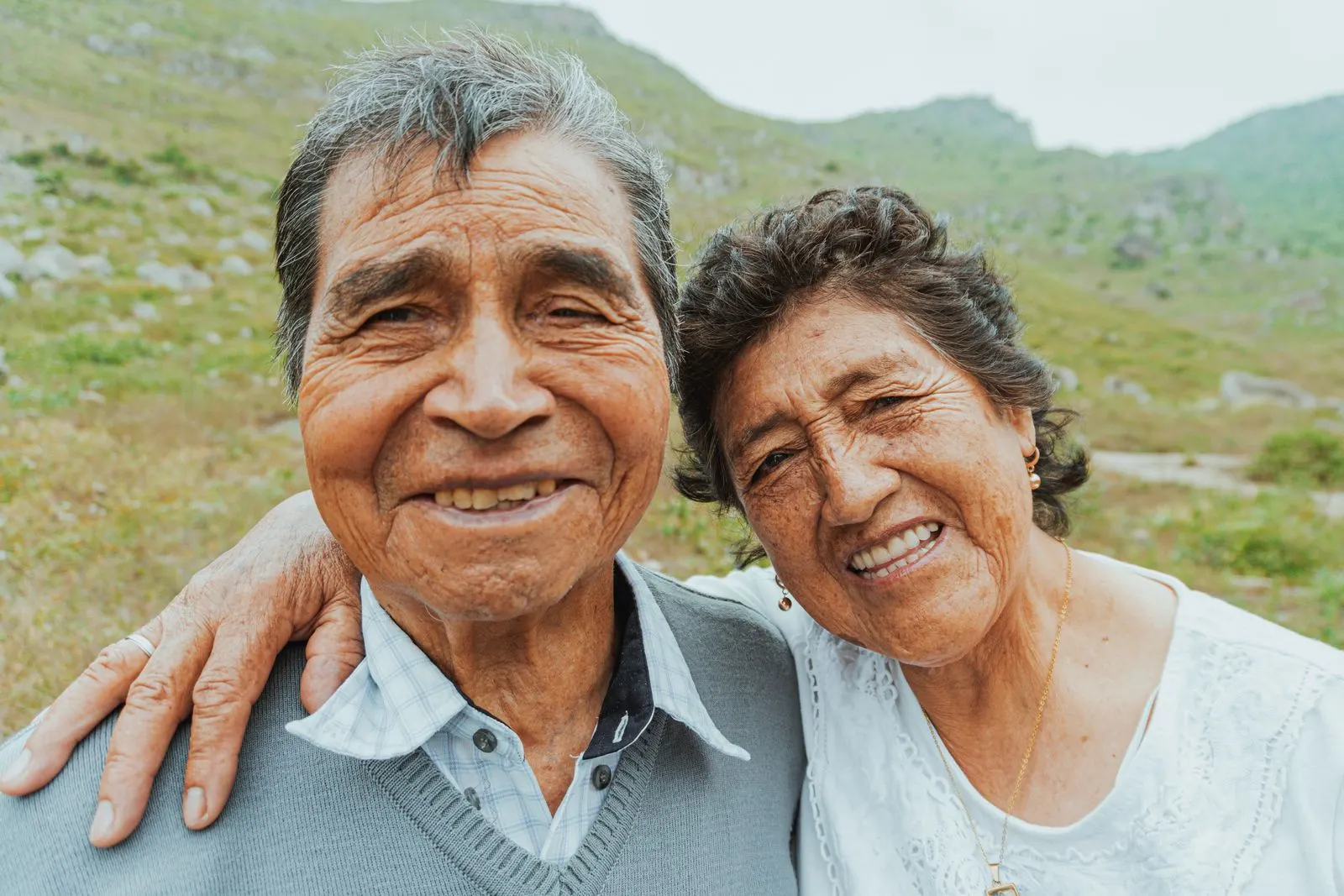 A smiling older couple arm in arm on a grassy hillside
