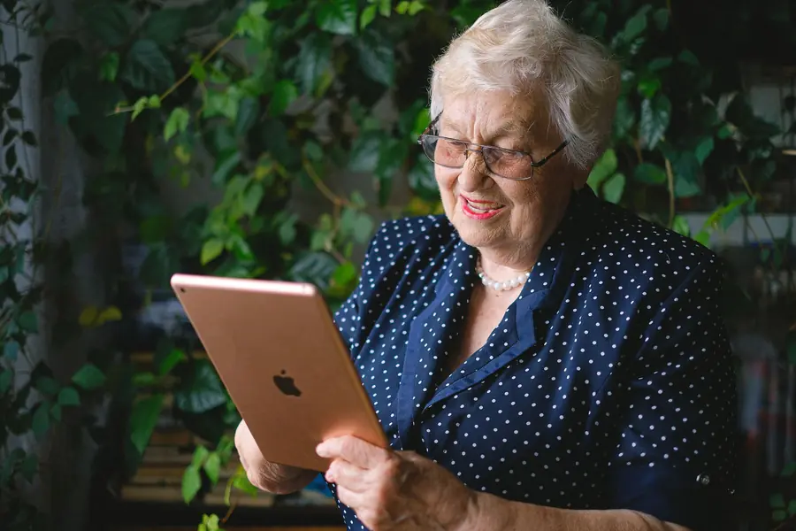 Smiling older woman in glasses on a video call on her tablet outdoors